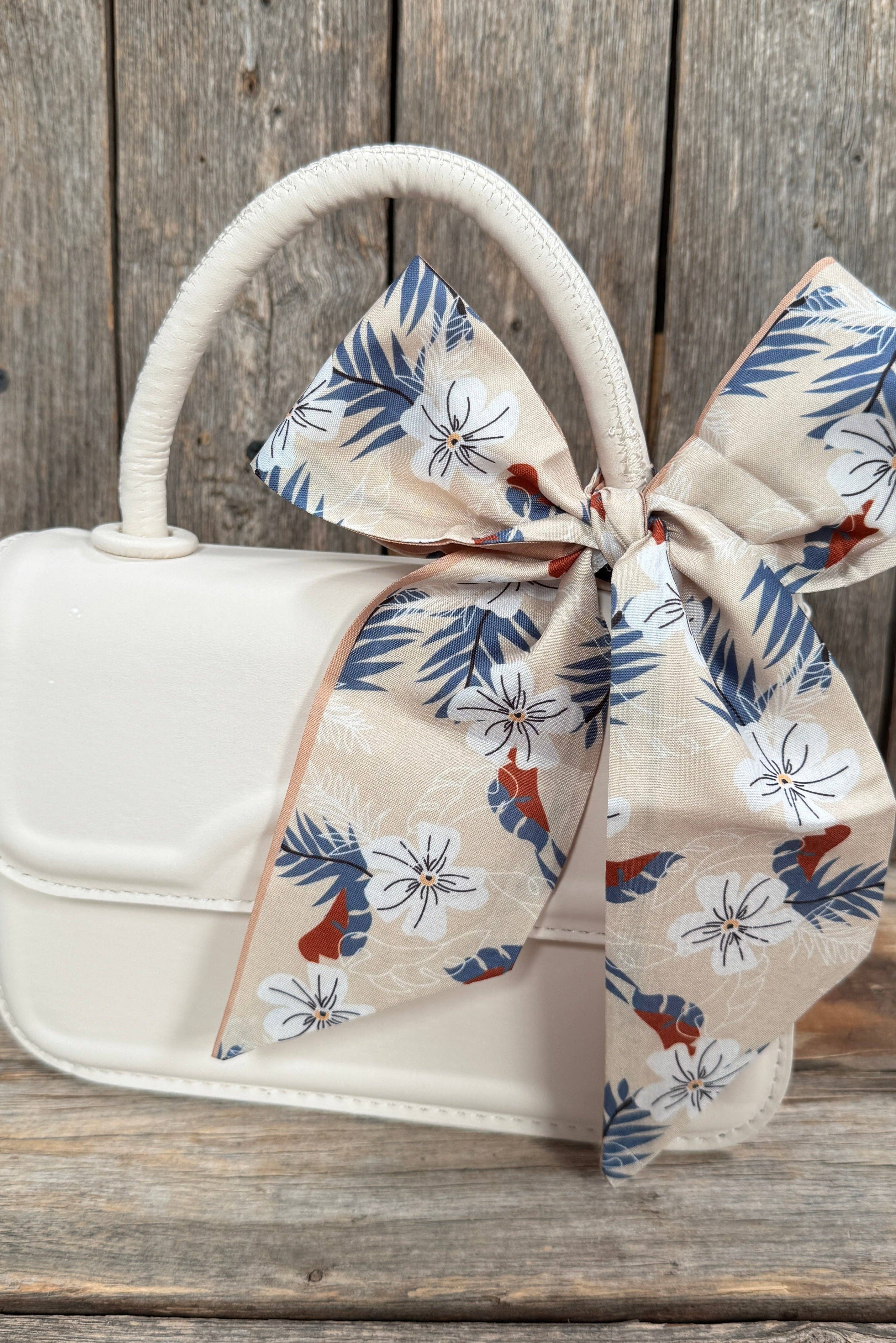 White handbag with a floral scarf ribbon on a wooden surface