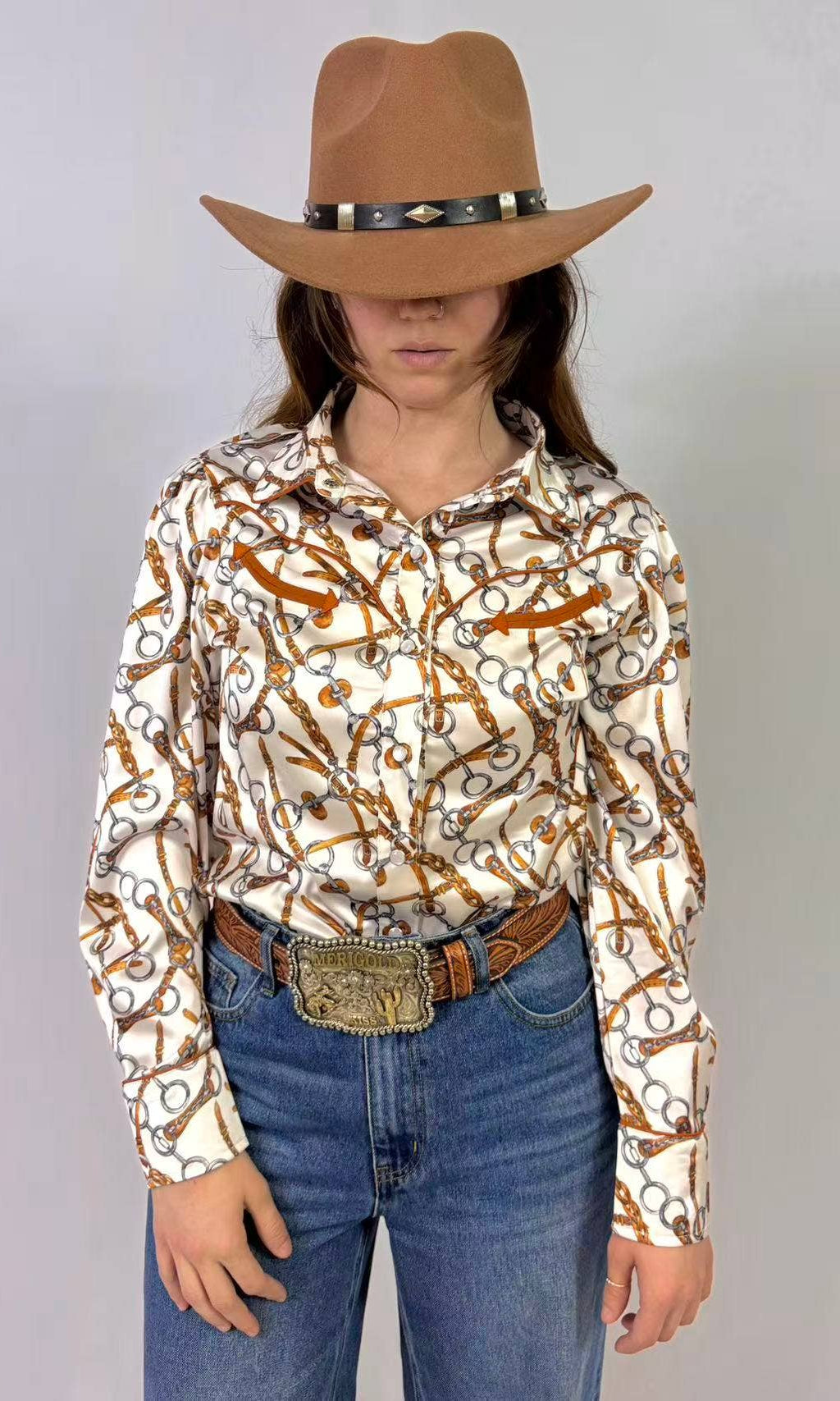 Person wearing a patterned shirt, jeans, and a cowboy hat with a belt on a plain background