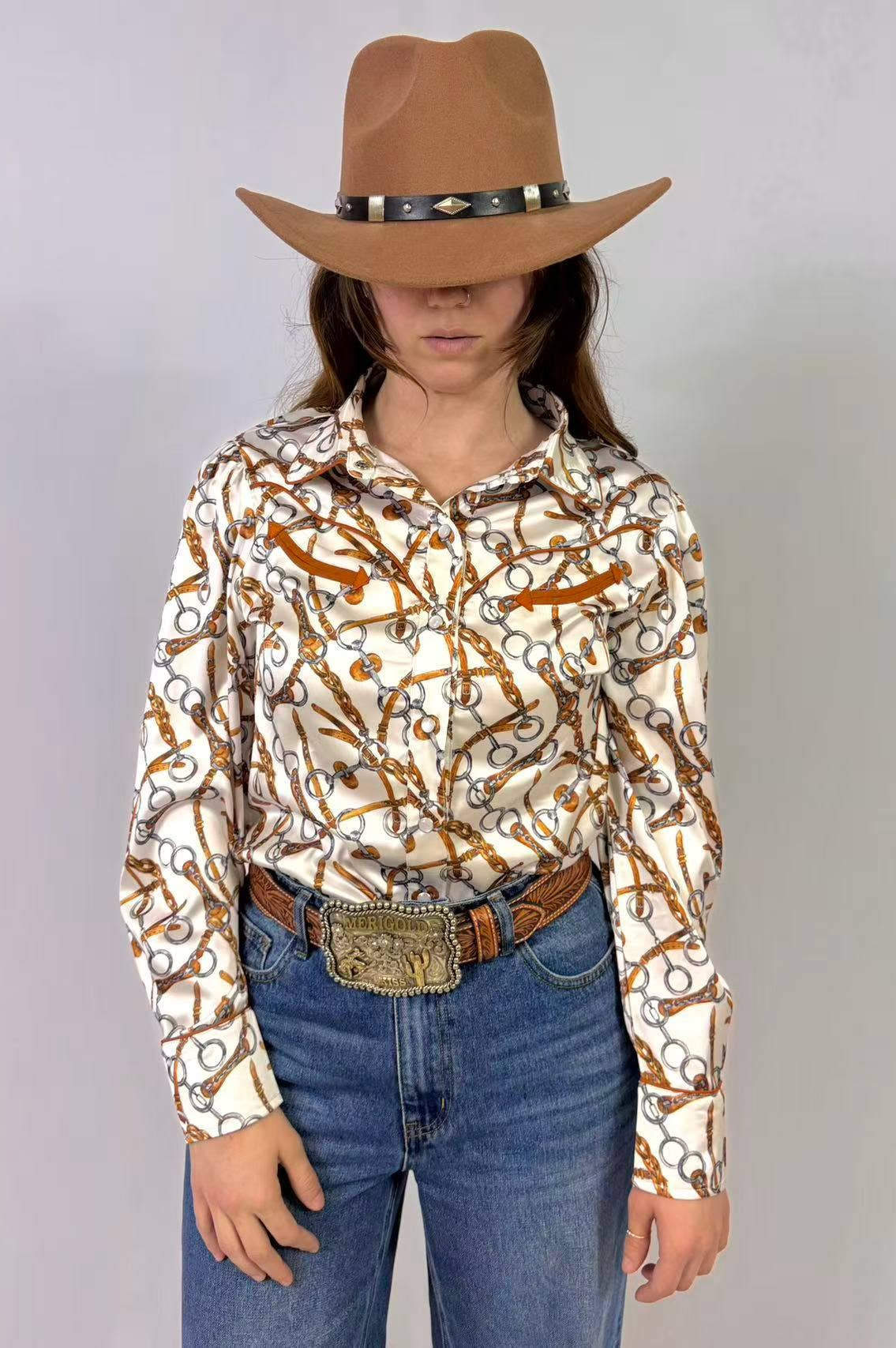 Person wearing a patterned shirt, jeans, and a cowboy hat with a belt on a plain background