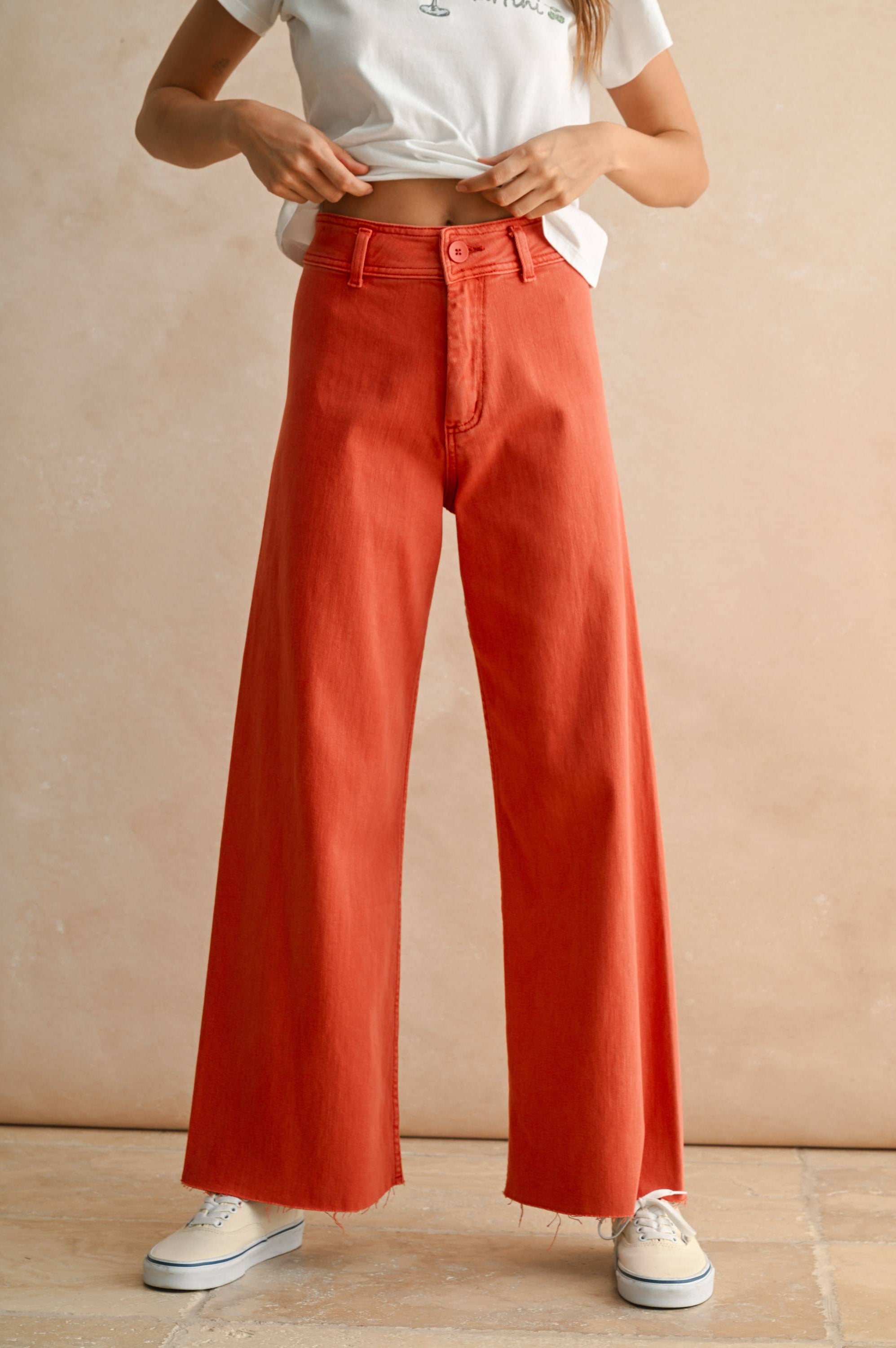 Person wearing burnt orange wide-leg pants and a white crop top against a beige background