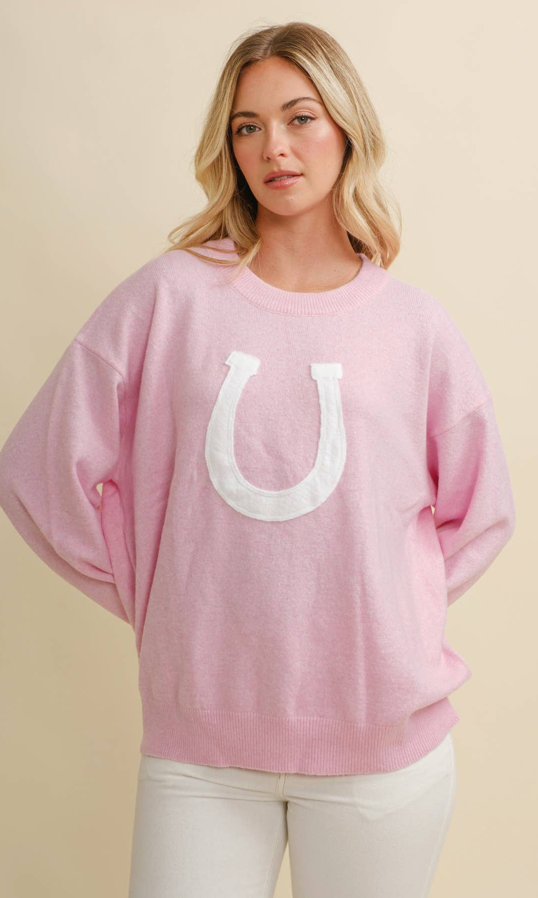 Woman wearing a pink sweater with a white horseshoe design on a beige background