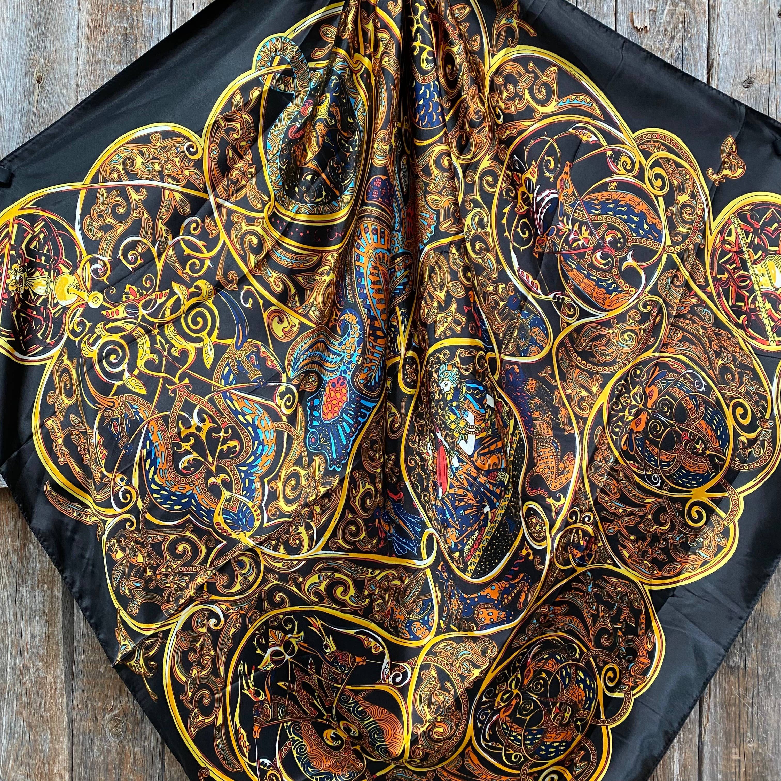 Decorative scarf with intricate gold, blue, and red patterns on a black background.