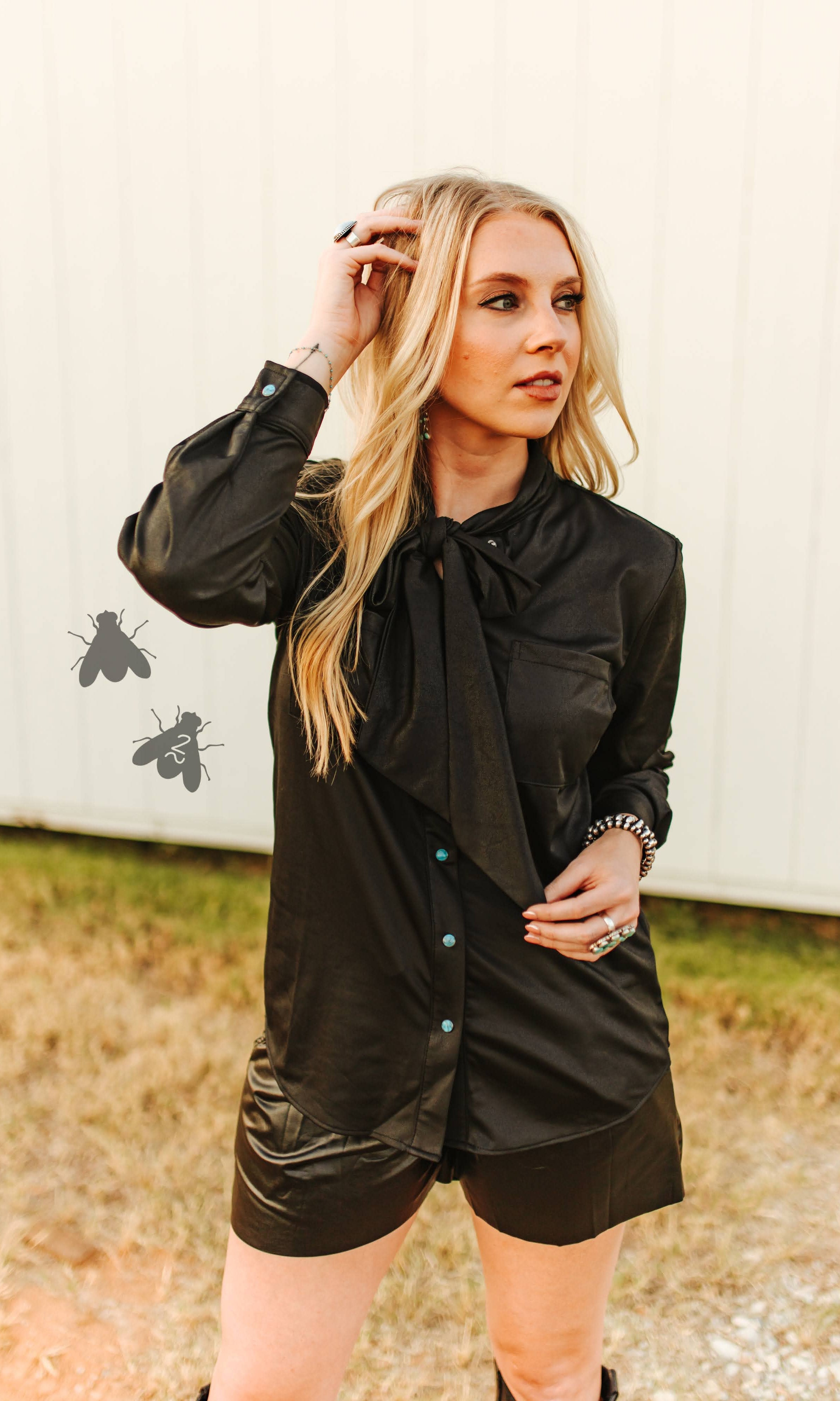 Woman wearing a black outfit with a bow tie against a white wall.
