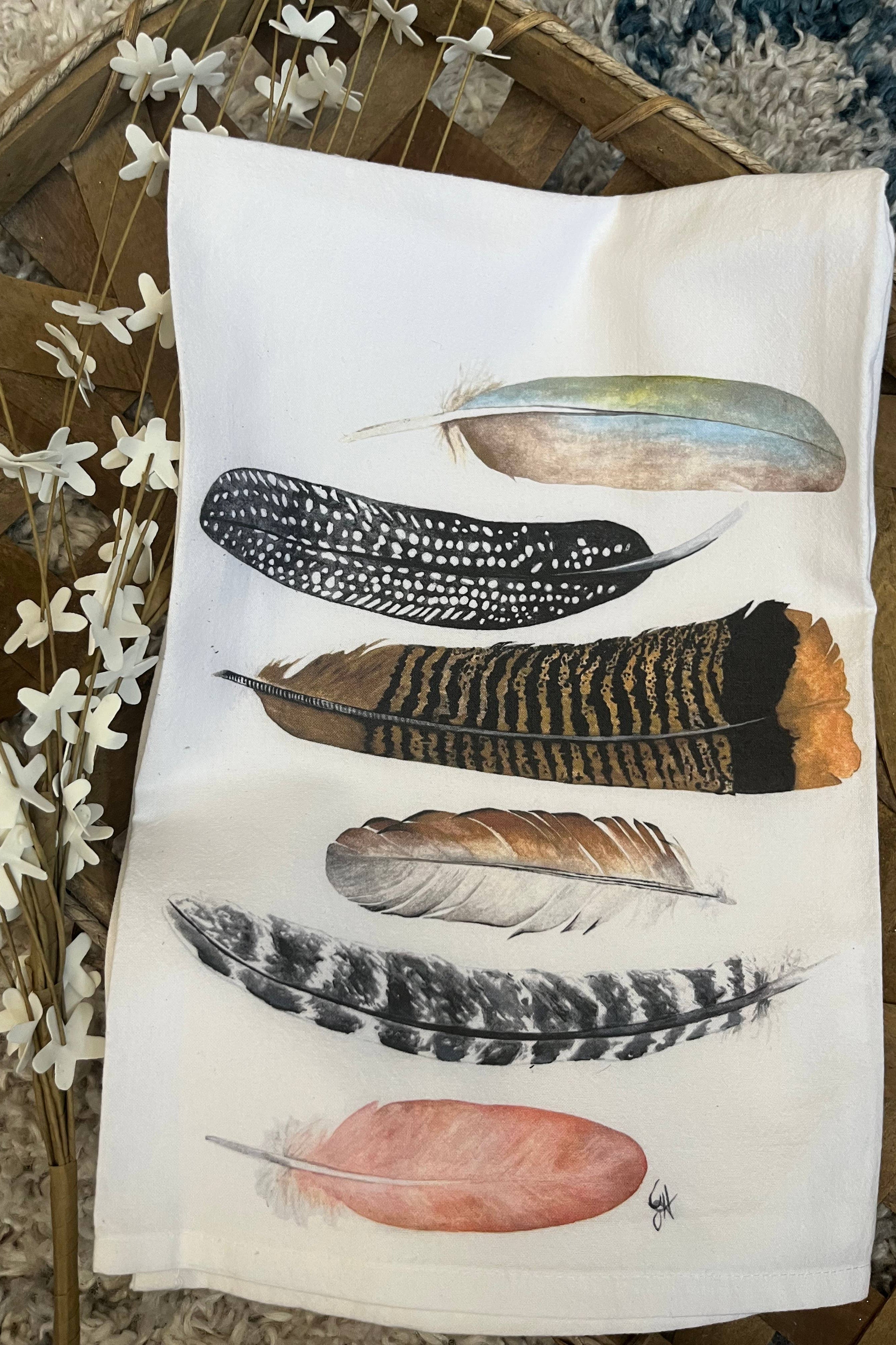 Tea towel with feather designs on a wooden surface with flowers.