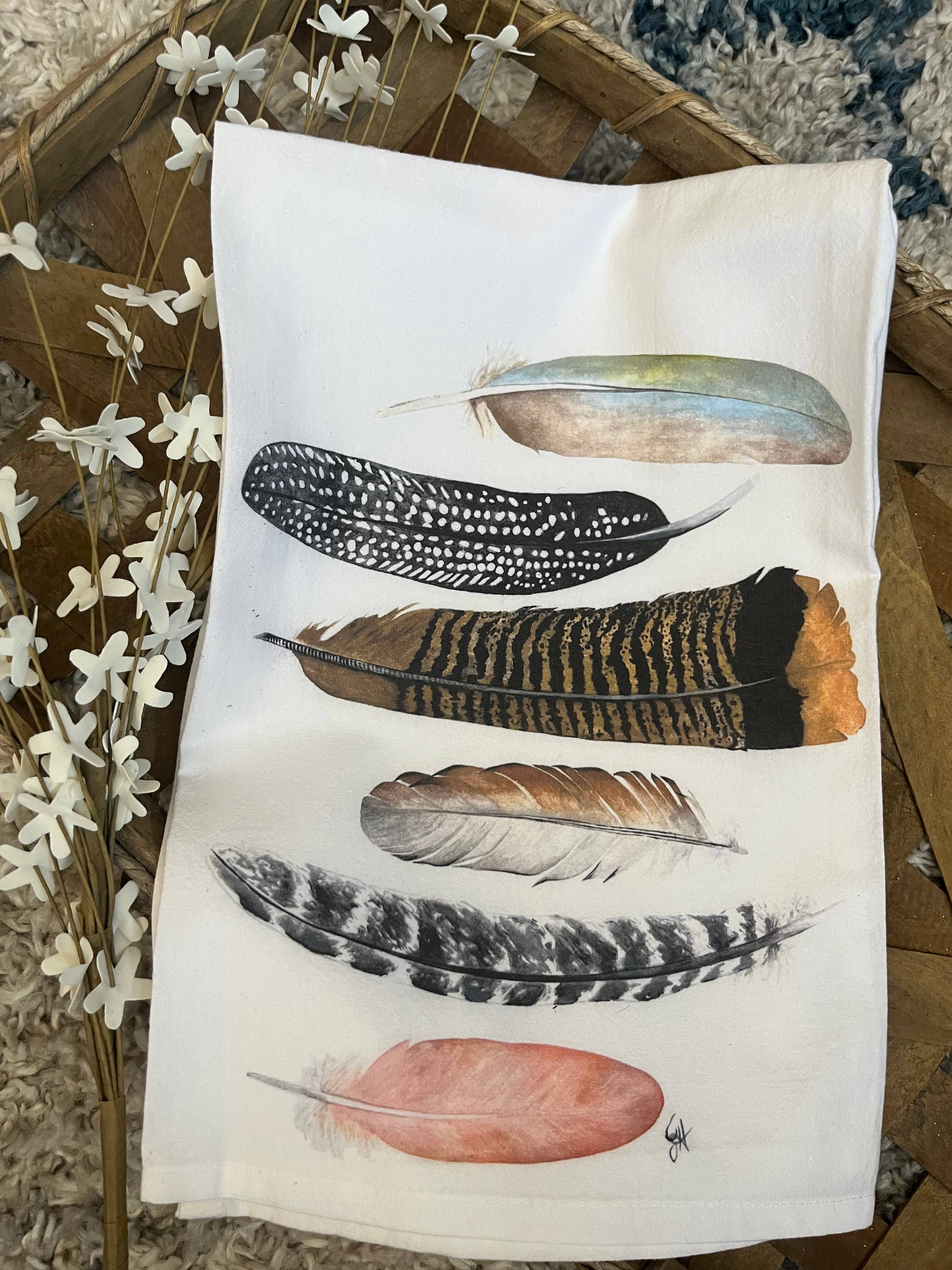 Tea towel with feather designs on a wooden surface with flowers.