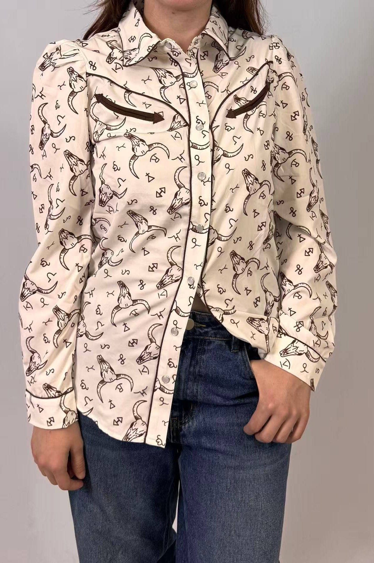 Person wearing a patterned shirt with long sleeves and jeans on a plain background
