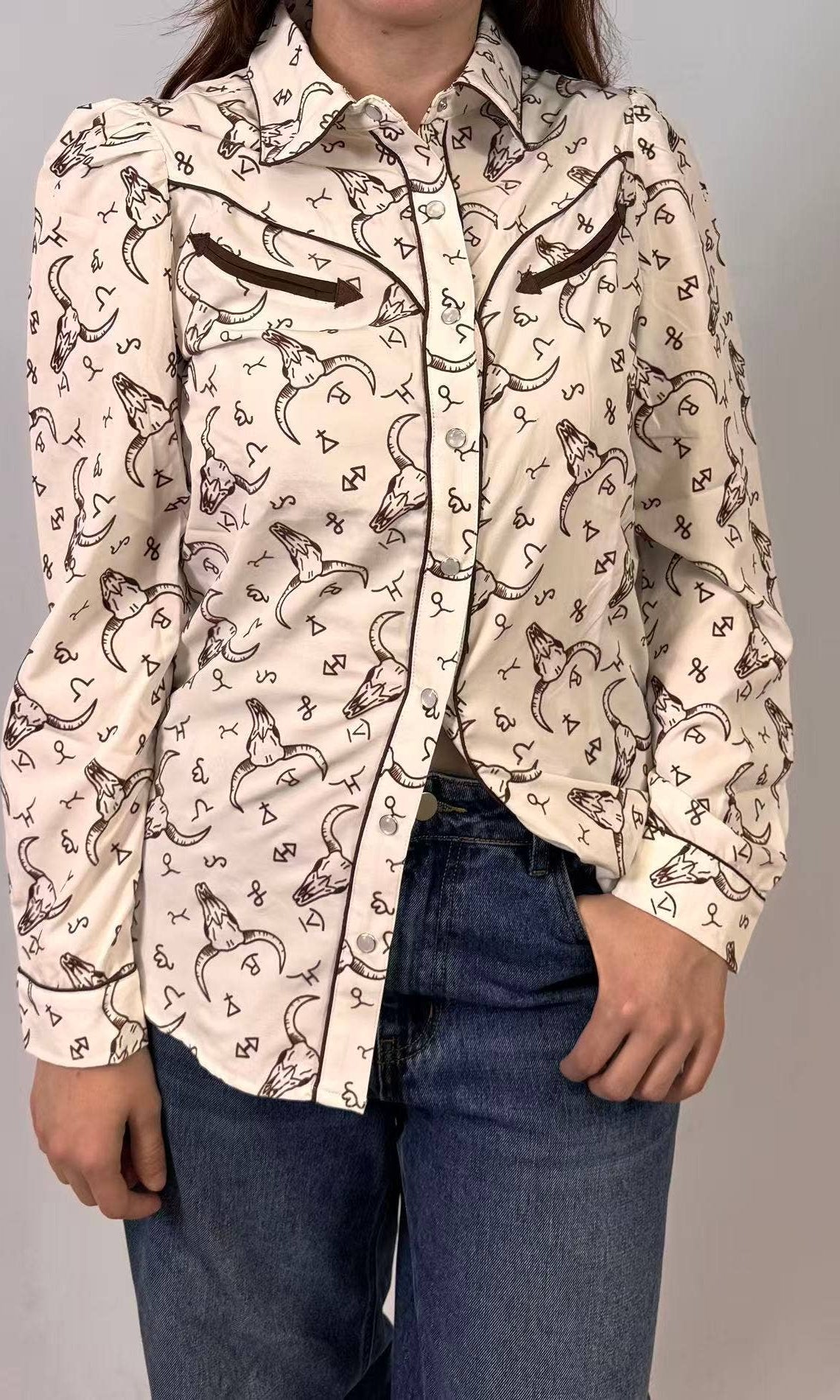 Person wearing a patterned shirt with long sleeves and jeans on a plain background