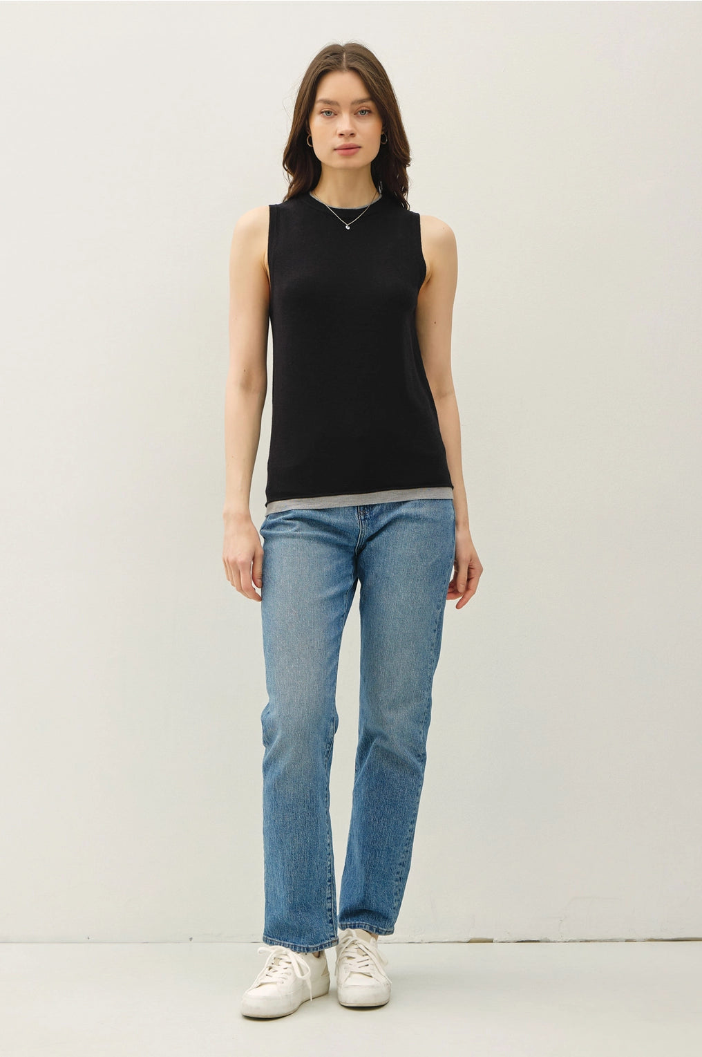 Woman wearing a black sleeveless top and blue jeans on a white background