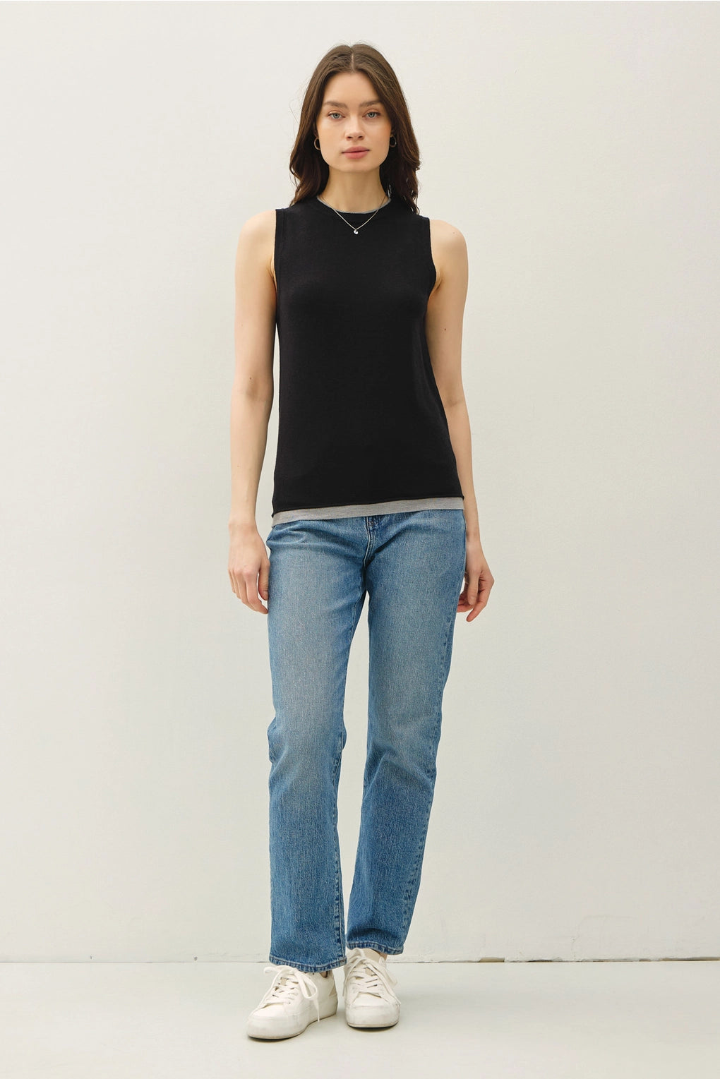 Woman wearing a black sleeveless top and blue jeans on a white background