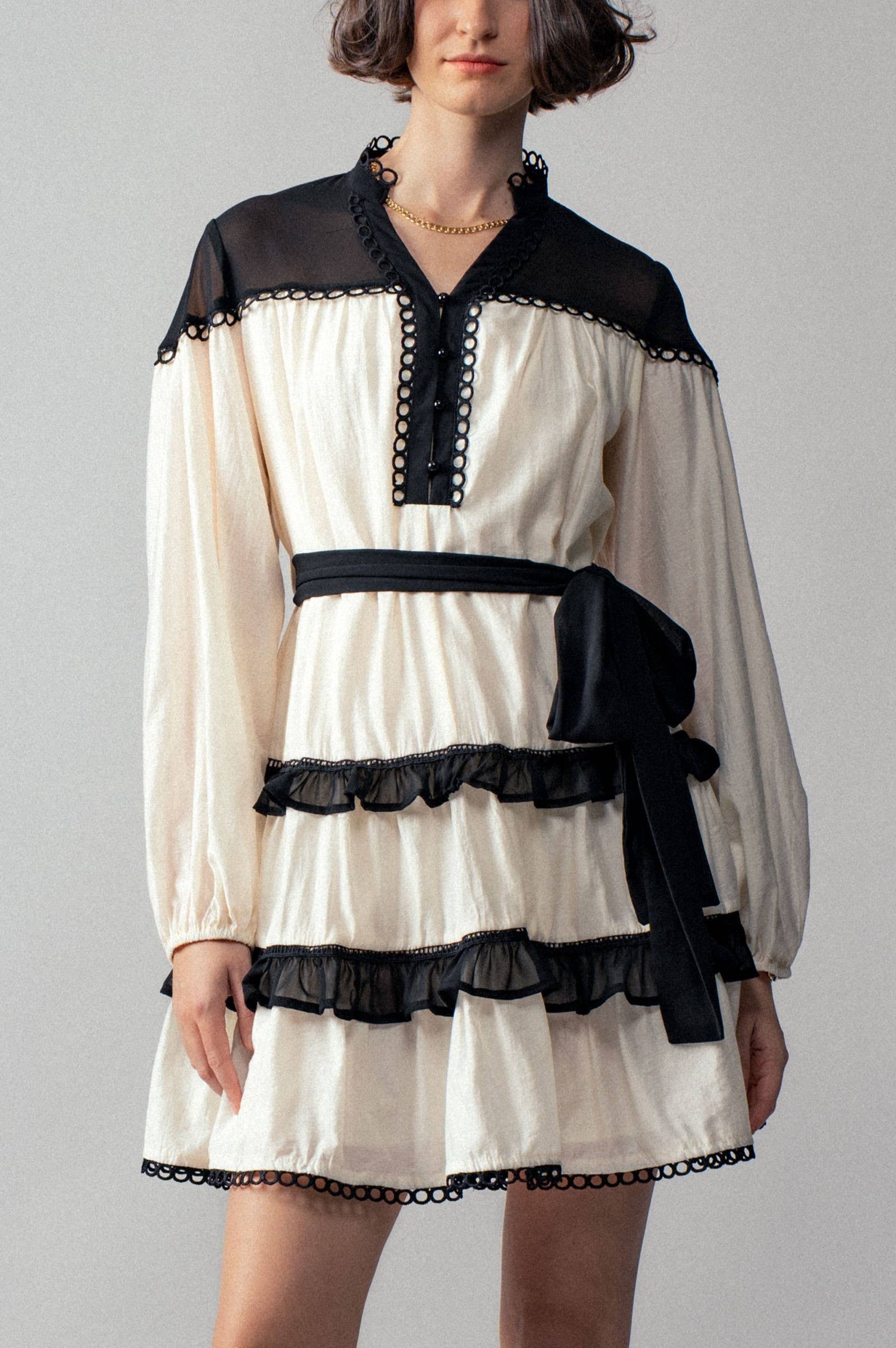 White dress with black ruffle accents worn by a person on a plain background