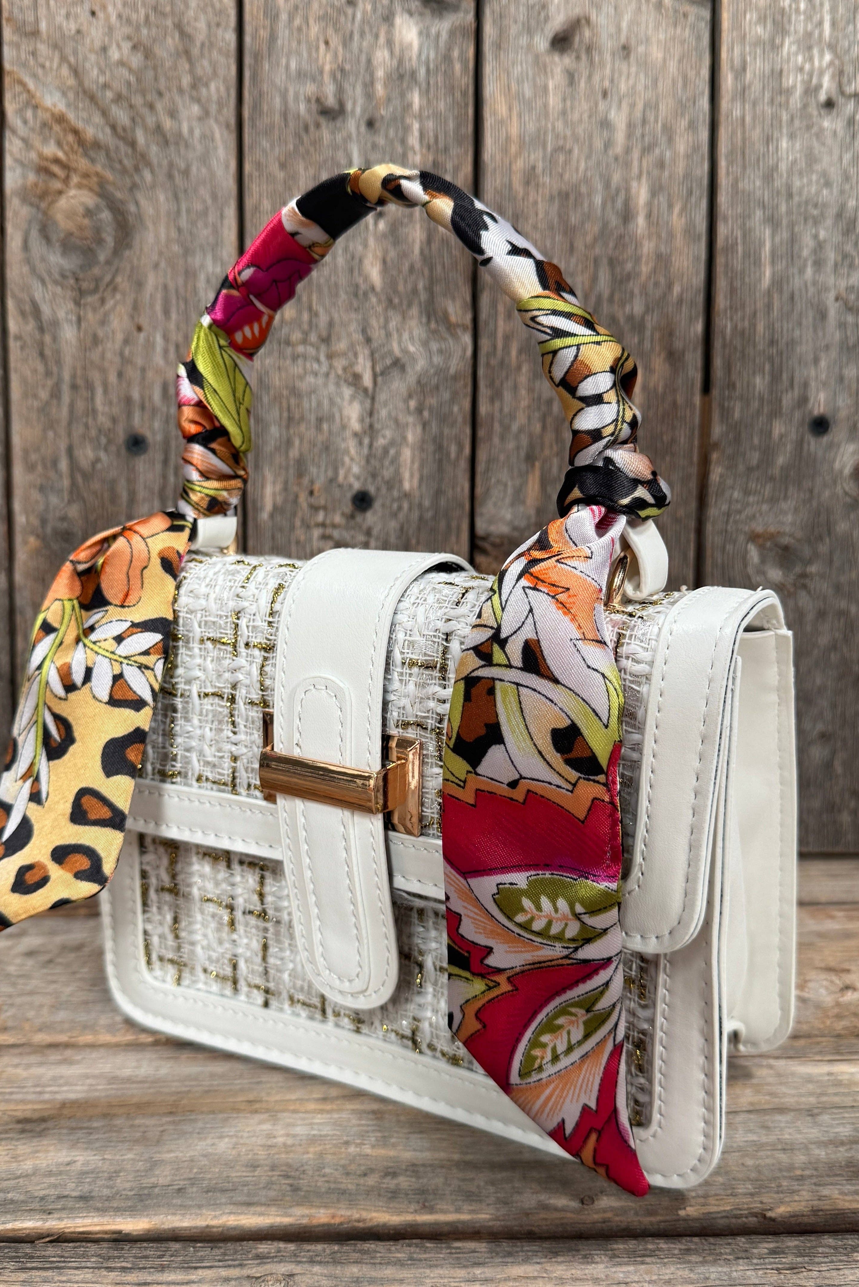 White handbag with a colorful scarf draped over it on a wooden surface