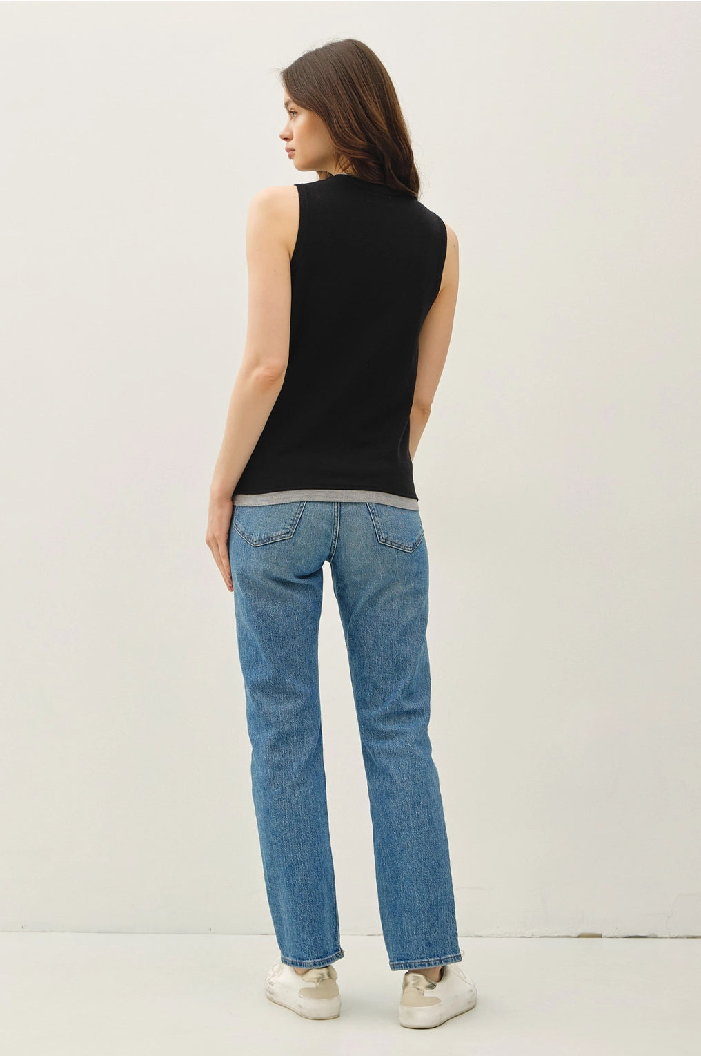 Back View Woman wearing a black sleeveless top and blue jeans on a white background