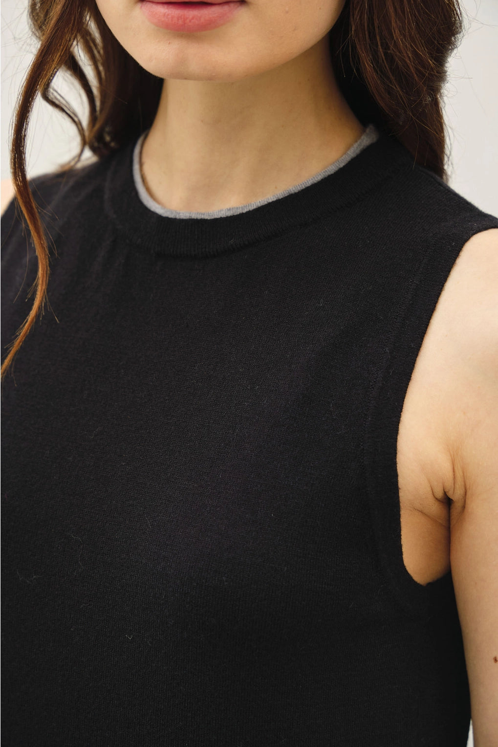 up close of the black top with grey trim sleeveless top worn by a person with a neutral background