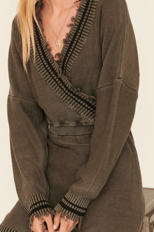 Person wearing a olive green sweater dress with striped cuffs and hem on a plain background