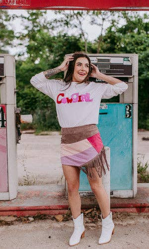 Woman posing in front of a vintage gas pump wearing a 'Cowgirl' sweatshirt.