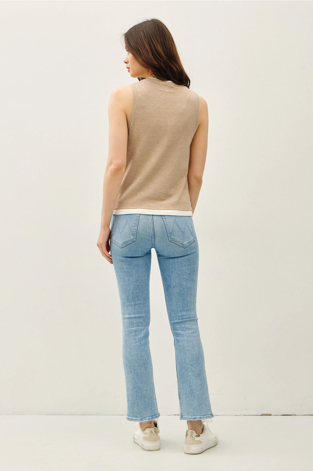 Woman wearing a top sleeveless top with lighter contrasting band at the bottom of the tops and blue jeans on a plain background