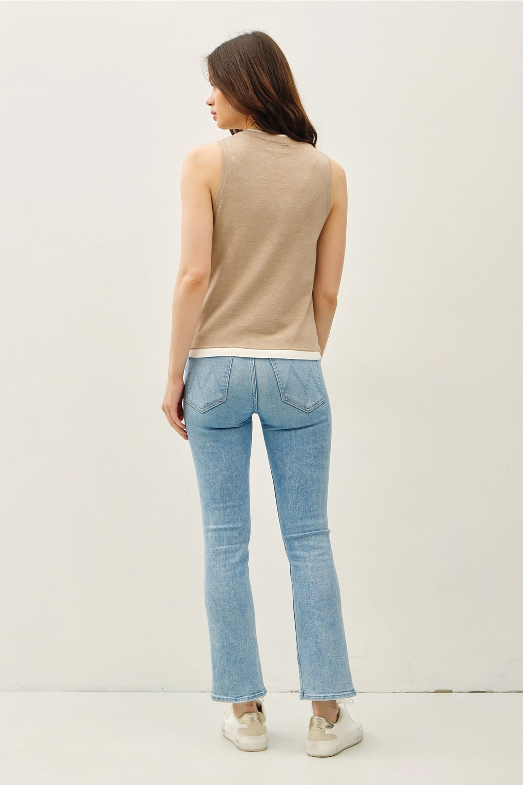 Woman wearing a top sleeveless top with lighter contrasting band at the bottom of the tops and blue jeans on a plain background