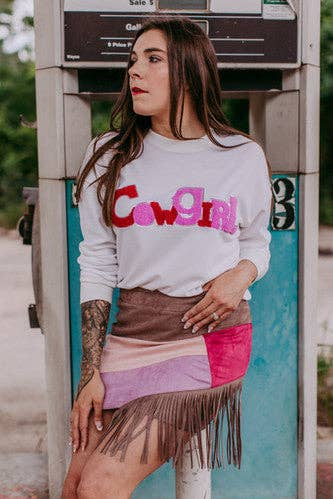 Woman wearing a white sweatshirt with colorful text and a patterned skirt standing next to a payphone.