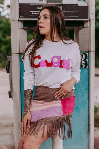 Woman wearing a white sweatshirt with colorful text and a patterned skirt standing next to a payphone.