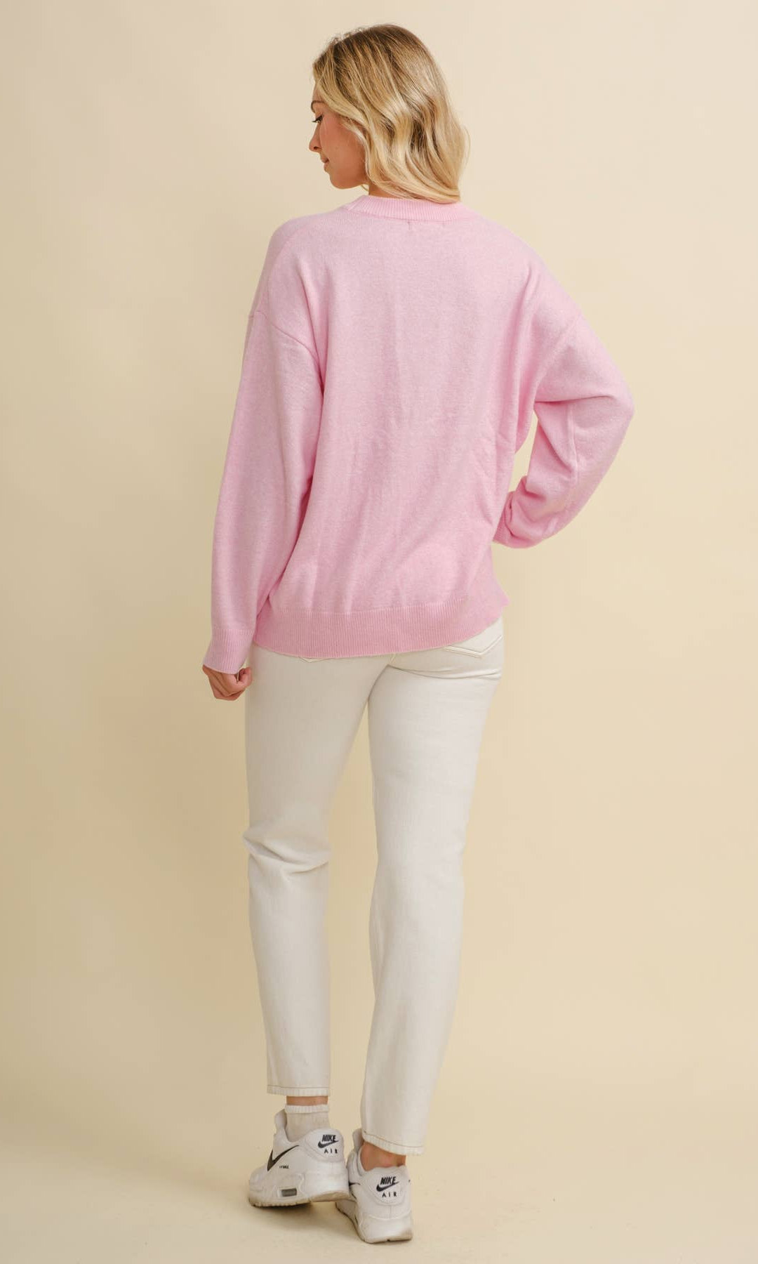 Woman wearing a pink long-sleeve sweater and white pants on a beige background