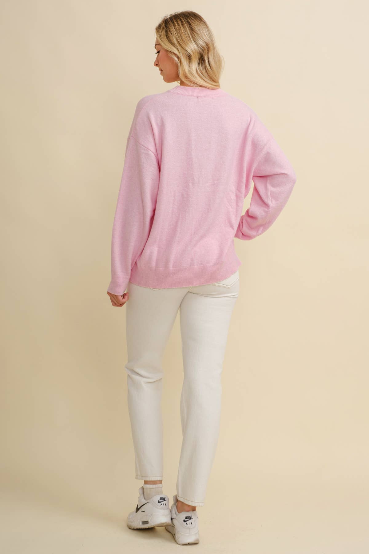 Woman wearing a pink long-sleeve sweater and white pants on a beige background