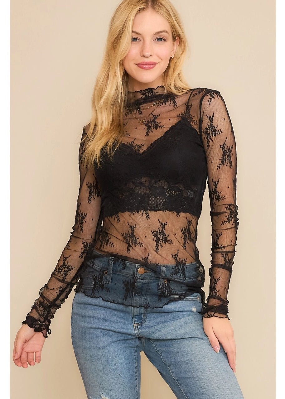 Woman wearing a sheer black top with lace details on a plain background