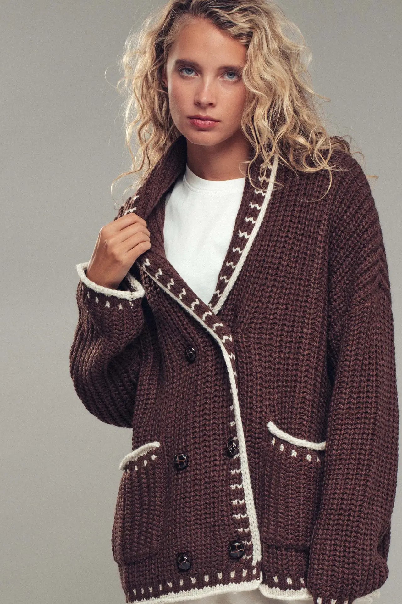 Woman wearing a brown knitted cardigan with white trim on a gray background
