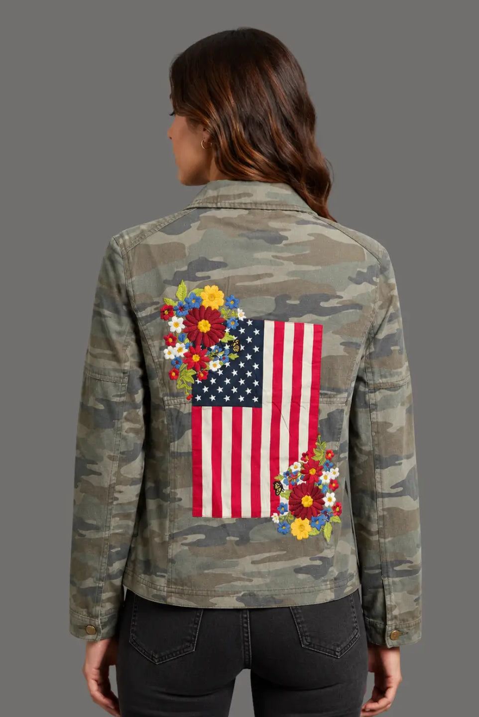 Camouflage jacket with American flag and floral design on the back, worn by a person.