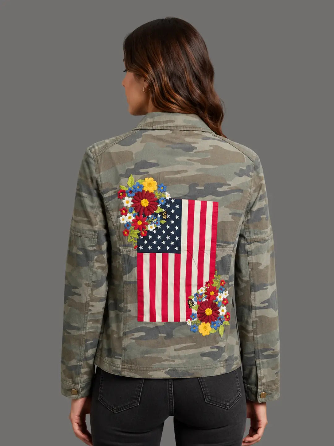 Camouflage jacket with American flag and floral design on the back, worn by a person.