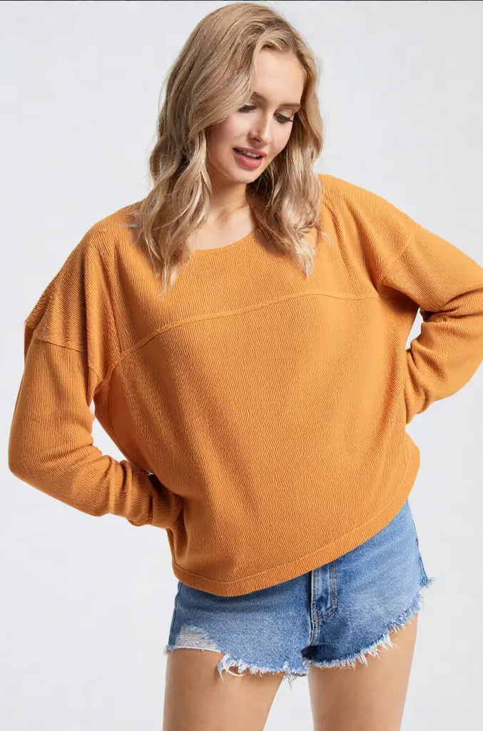 Woman wearing a mustard yellow sweater and denim shorts on a white background