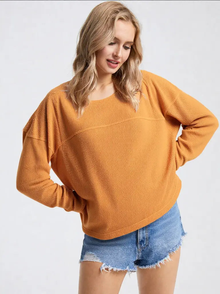 Woman wearing a mustard yellow sweater and denim shorts on a white background