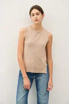 Woman wearing a beige sleeveless top and blue jeans against a white background