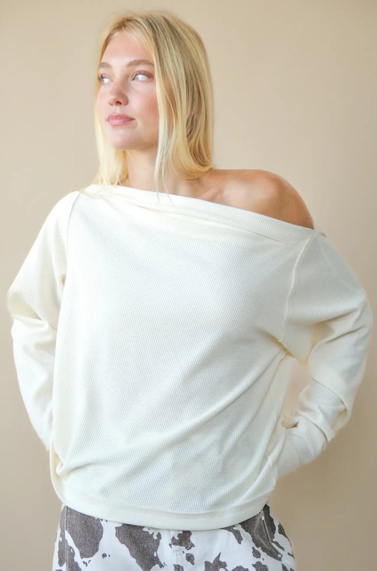 Front view of solid boat-neck cotton knit top worn slightly off-shoulder, long sleeves