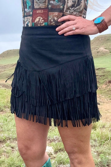 Person wearing a black fringe skirt with a patterned top in an outdoor setting