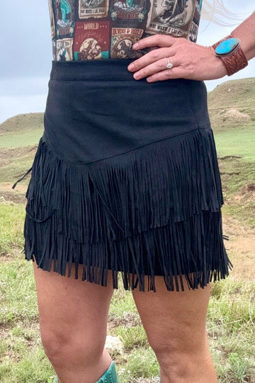 Person wearing a black fringe skirt with a patterned top in an outdoor setting
