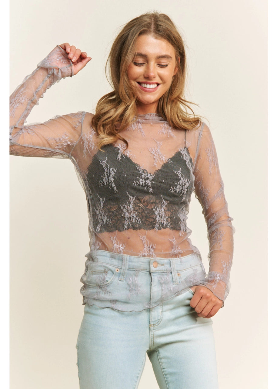 Woman wearing a sheer top with lace floral patterns in grey and light blue jeans on a beige background