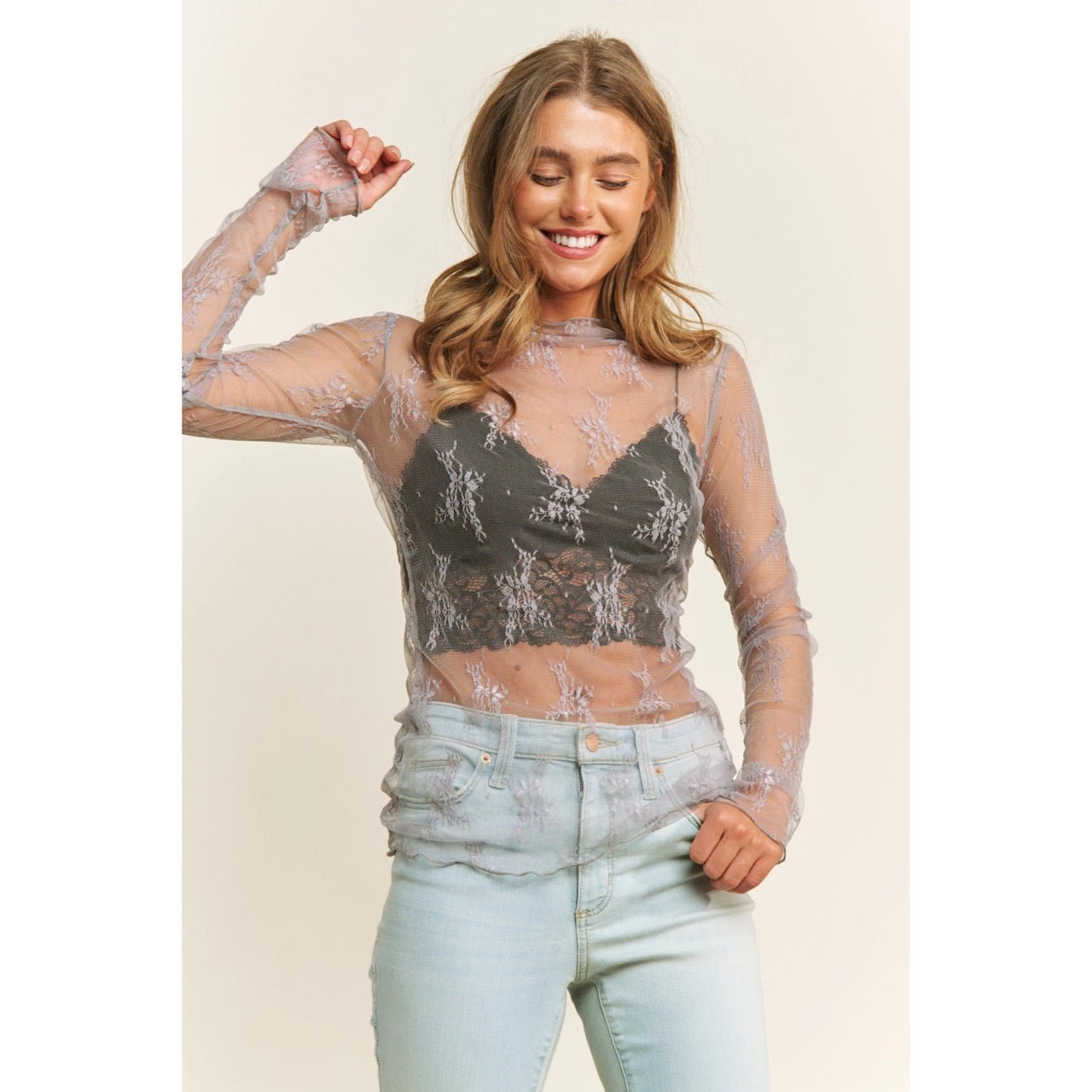 Woman wearing a sheer top with lace floral patterns in grey and light blue jeans on a beige background
