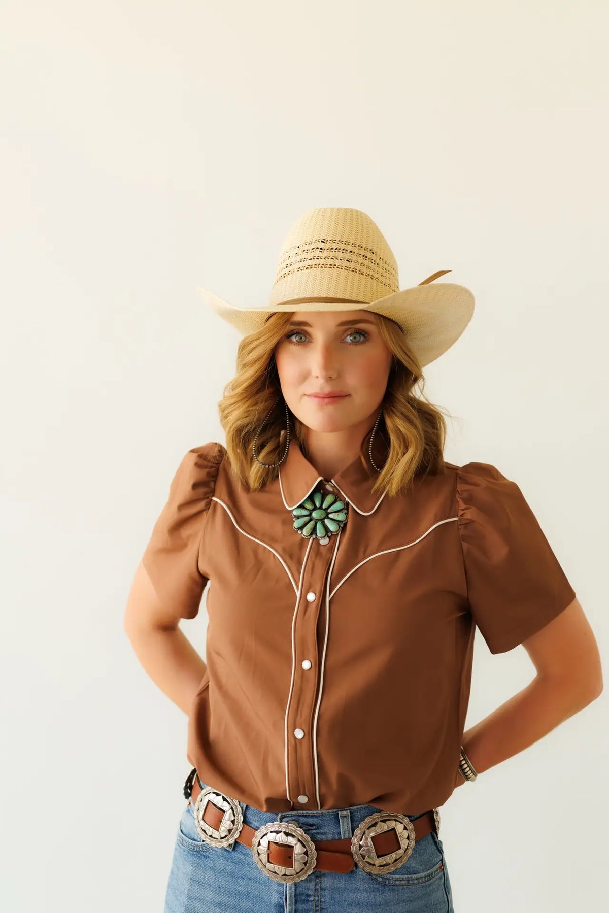 Women's brown Western pearl snap blouse featuring white contrast piping, classic Western yoke, puff sleeves, and a tailored fit.