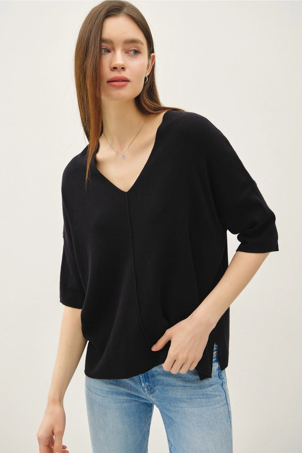 Woman wearing a black sweater and blue jeans against a white background