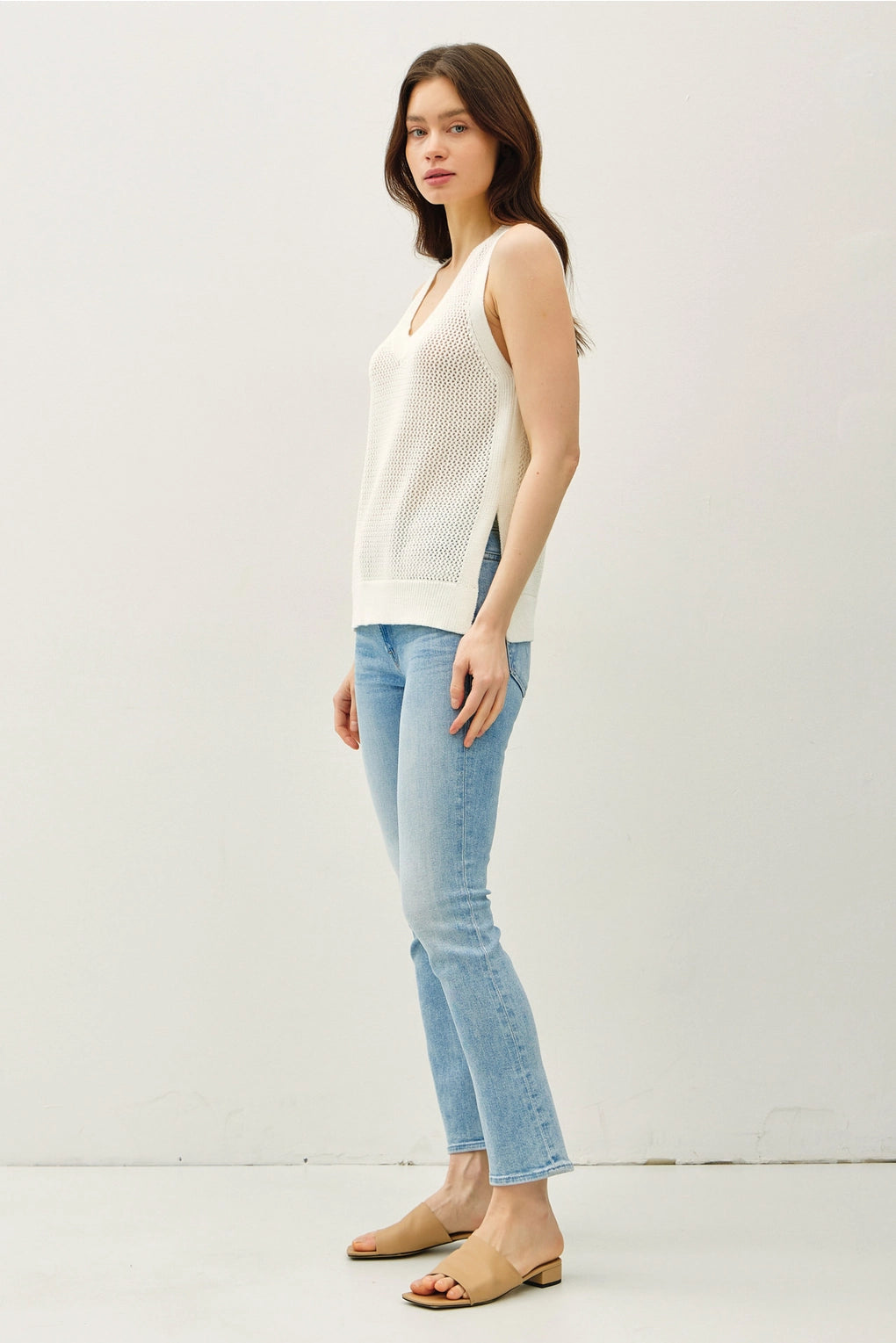 Woman wearing a white sleeveless top and light blue jeans against a white background