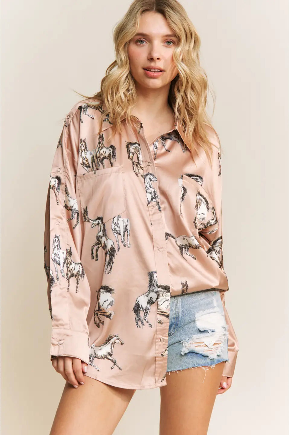 Woman wearing a light champagne shirt with horse print and denim shorts on a beige background