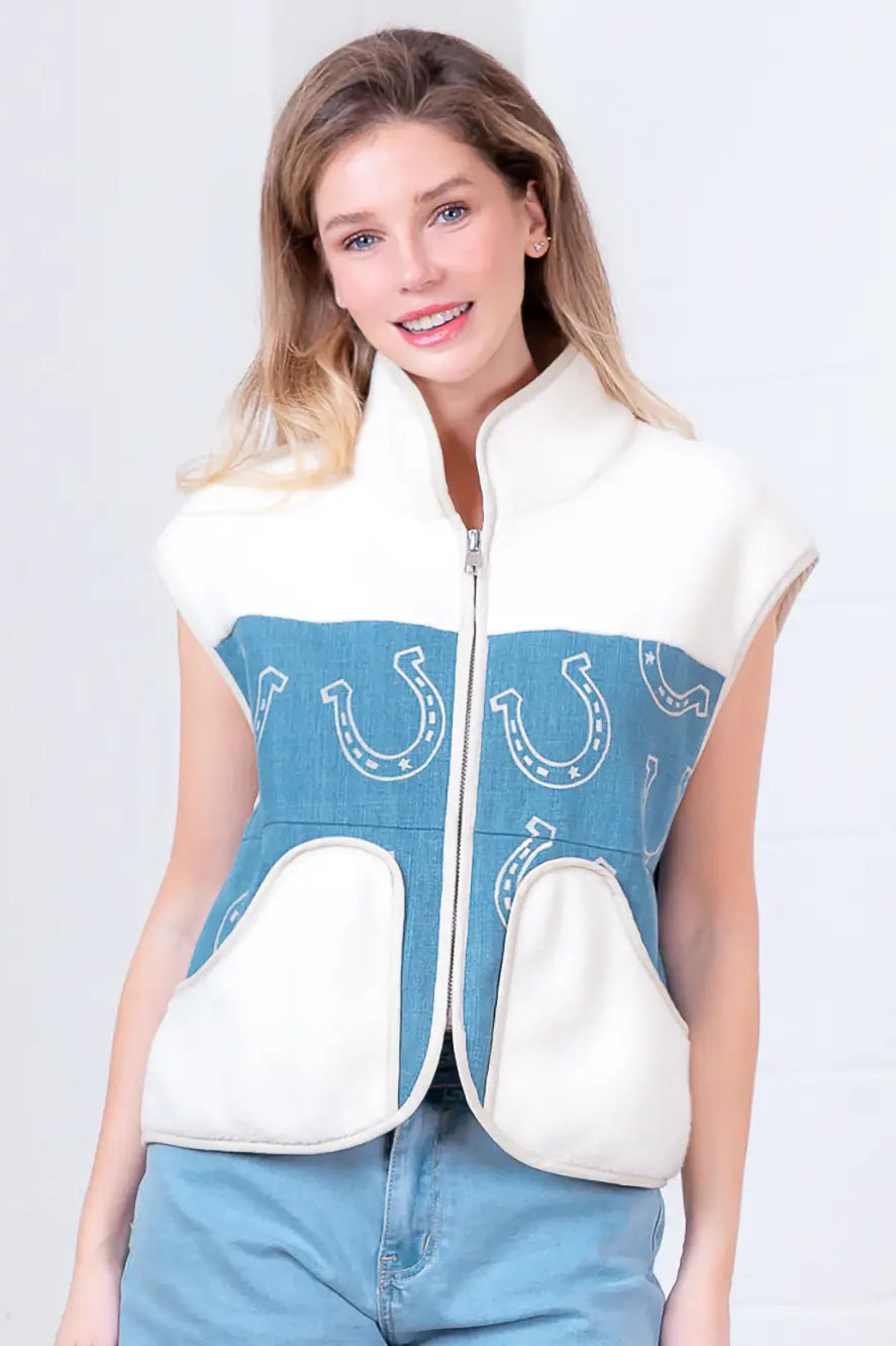 Model wearing indigo denim vest with white horseshoe print and faux-fur collar, zipped front, hands in pockets.”