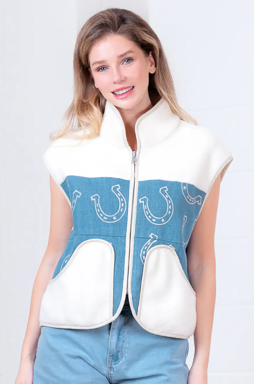 Model wearing indigo denim vest with white horseshoe print and faux-fur collar, zipped front, hands in pockets.”