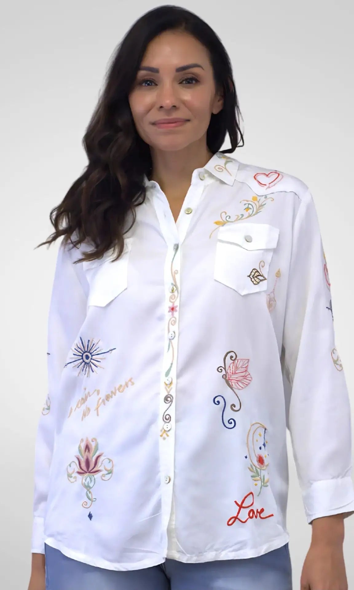 Woman wearing a white embroidered shirt against a plain background