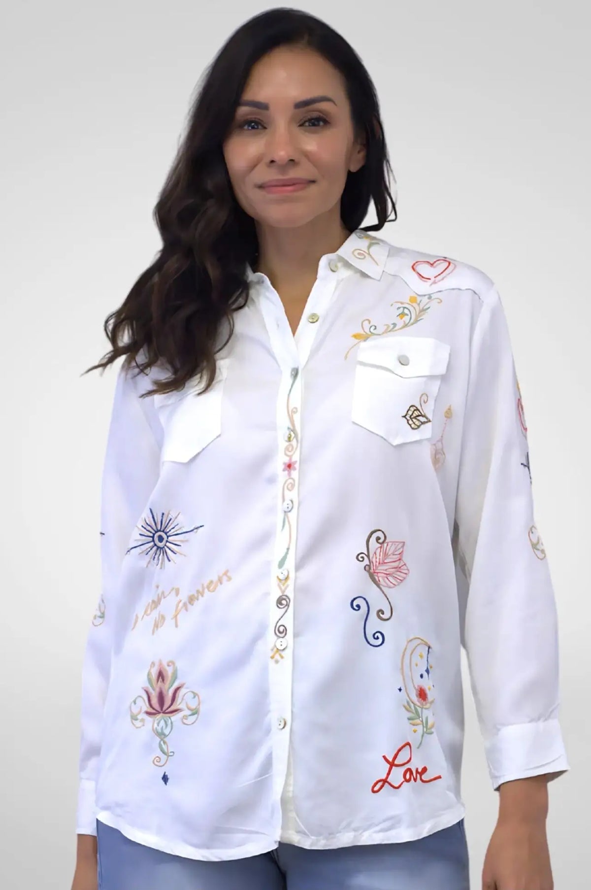 Woman wearing a white embroidered shirt against a plain background