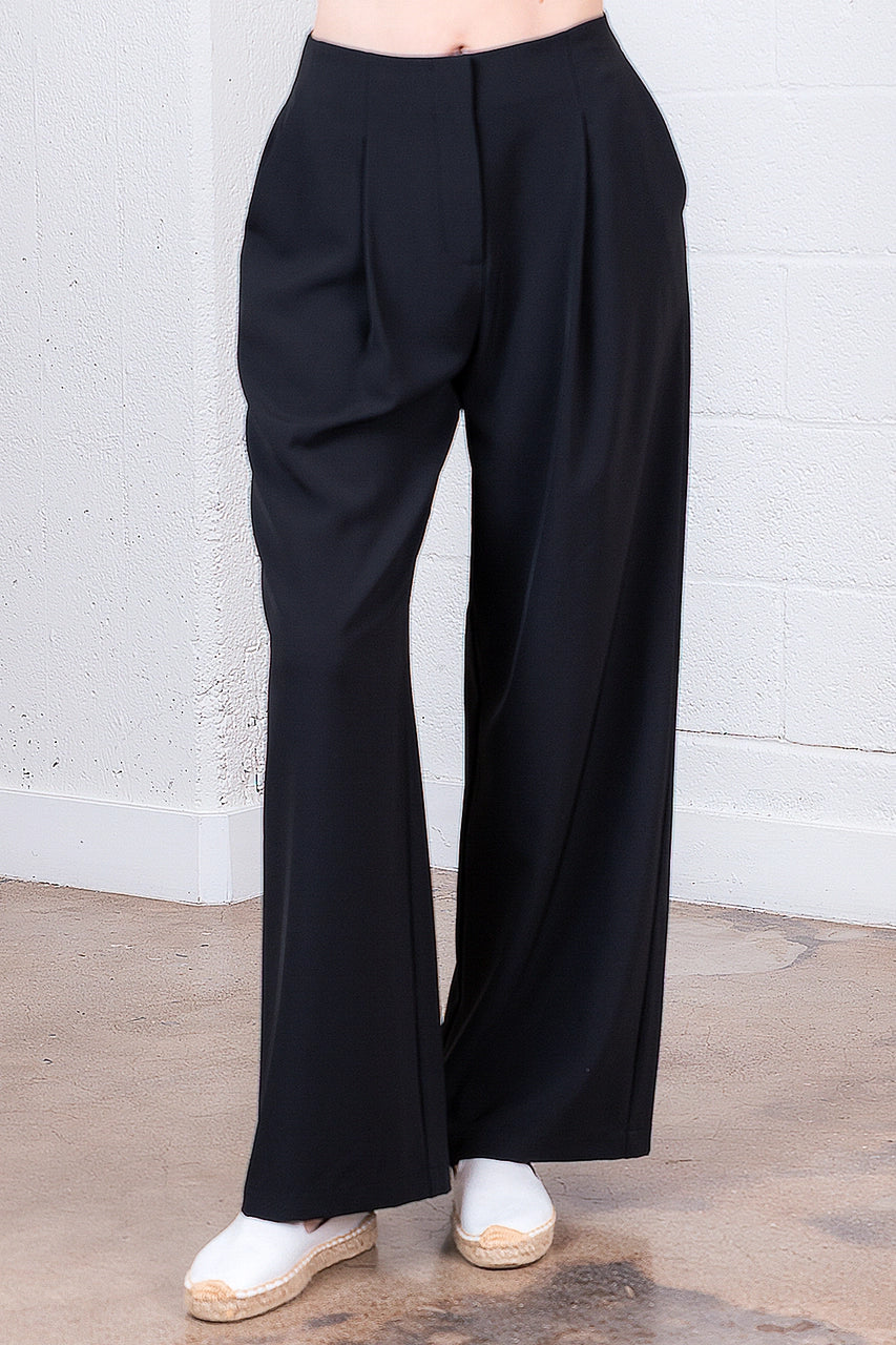 Black wide-leg pants worn by a person against a white brick wall.