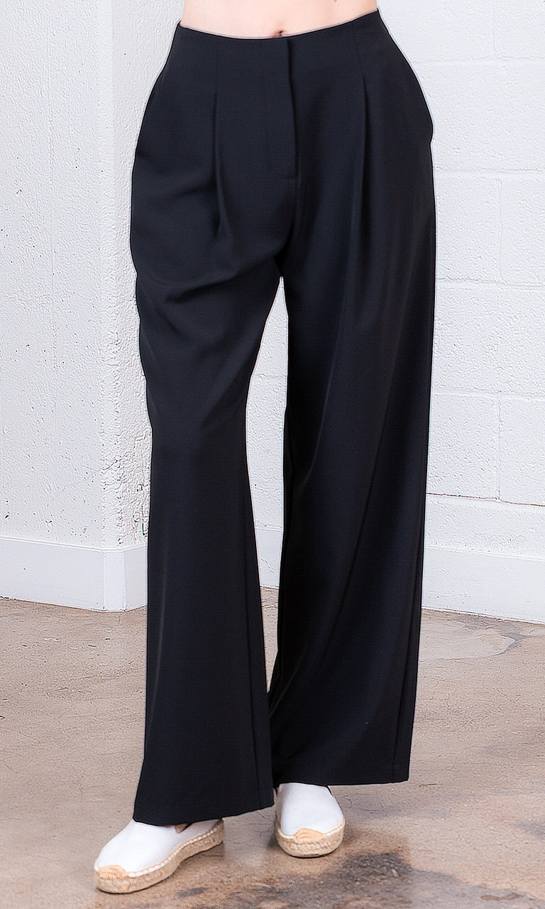 Black wide-leg pants worn by a person against a white brick wall.