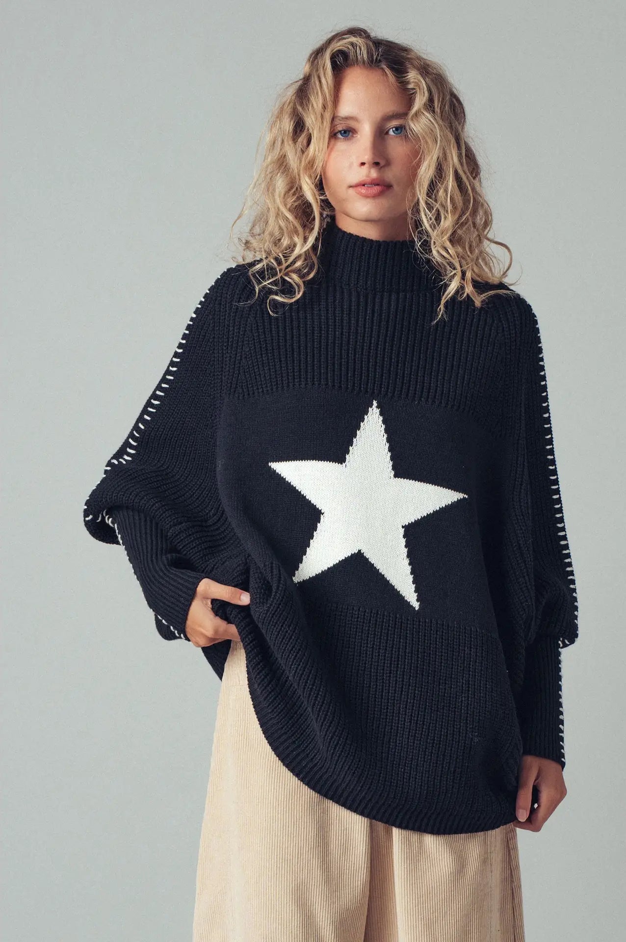 Person wearing a black sweater with a white star design on a plain background