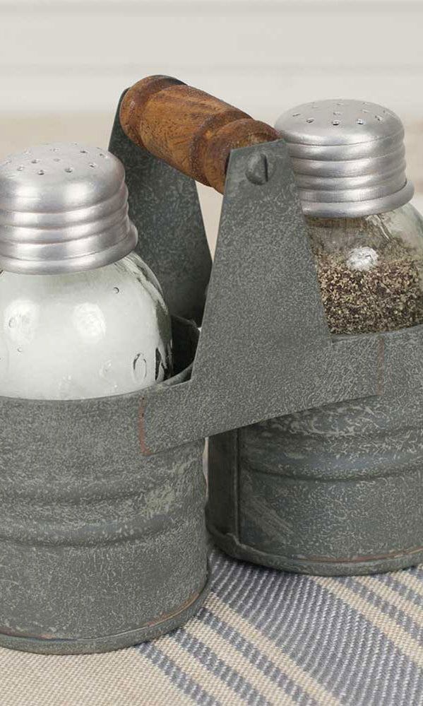 Two salt and pepper shakers in a metal caddy with a wood handle on a striped surface
