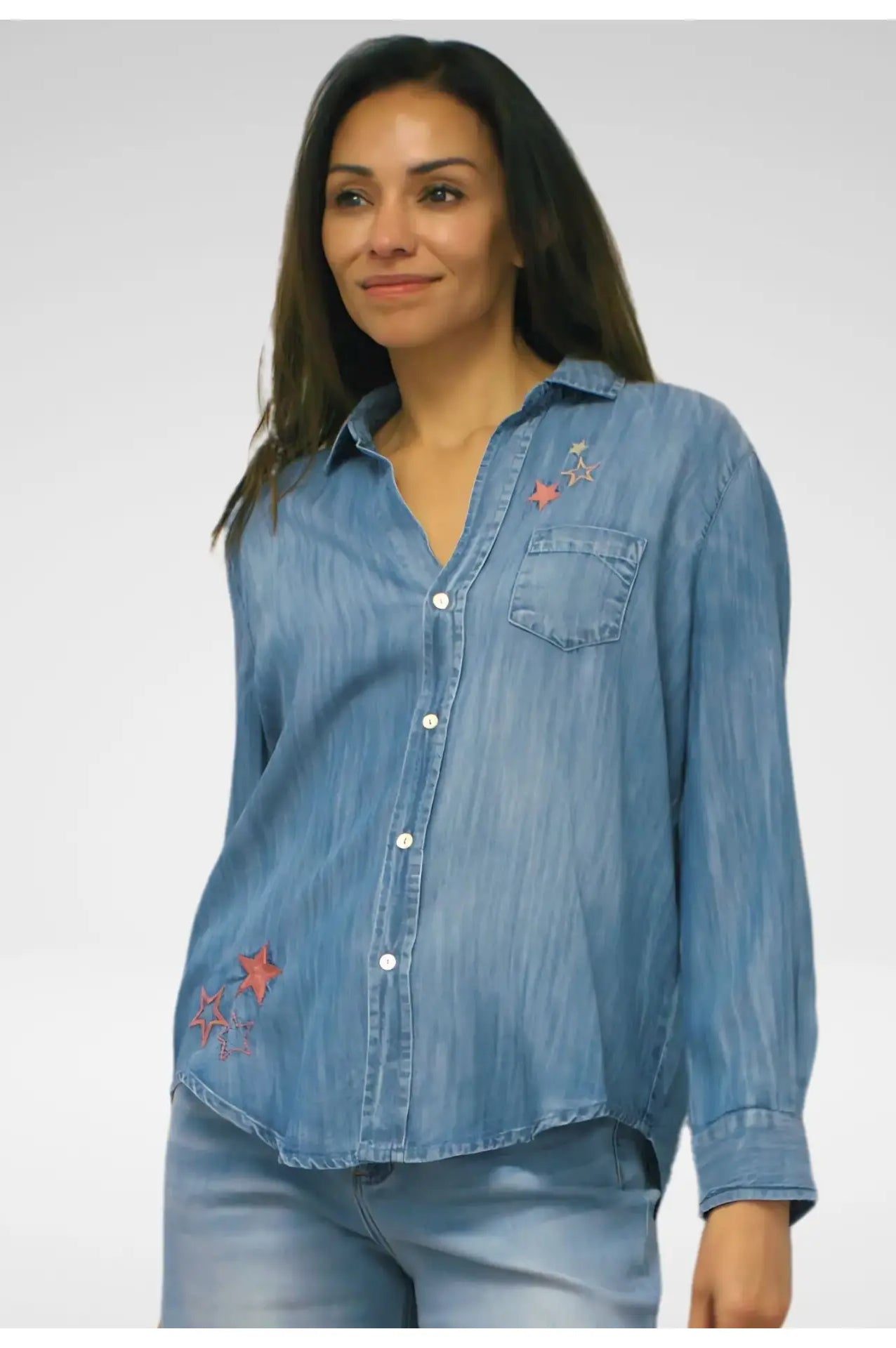 Woman wearing a long sleeve blue denim shirt with embroidered star patterns on a plain background